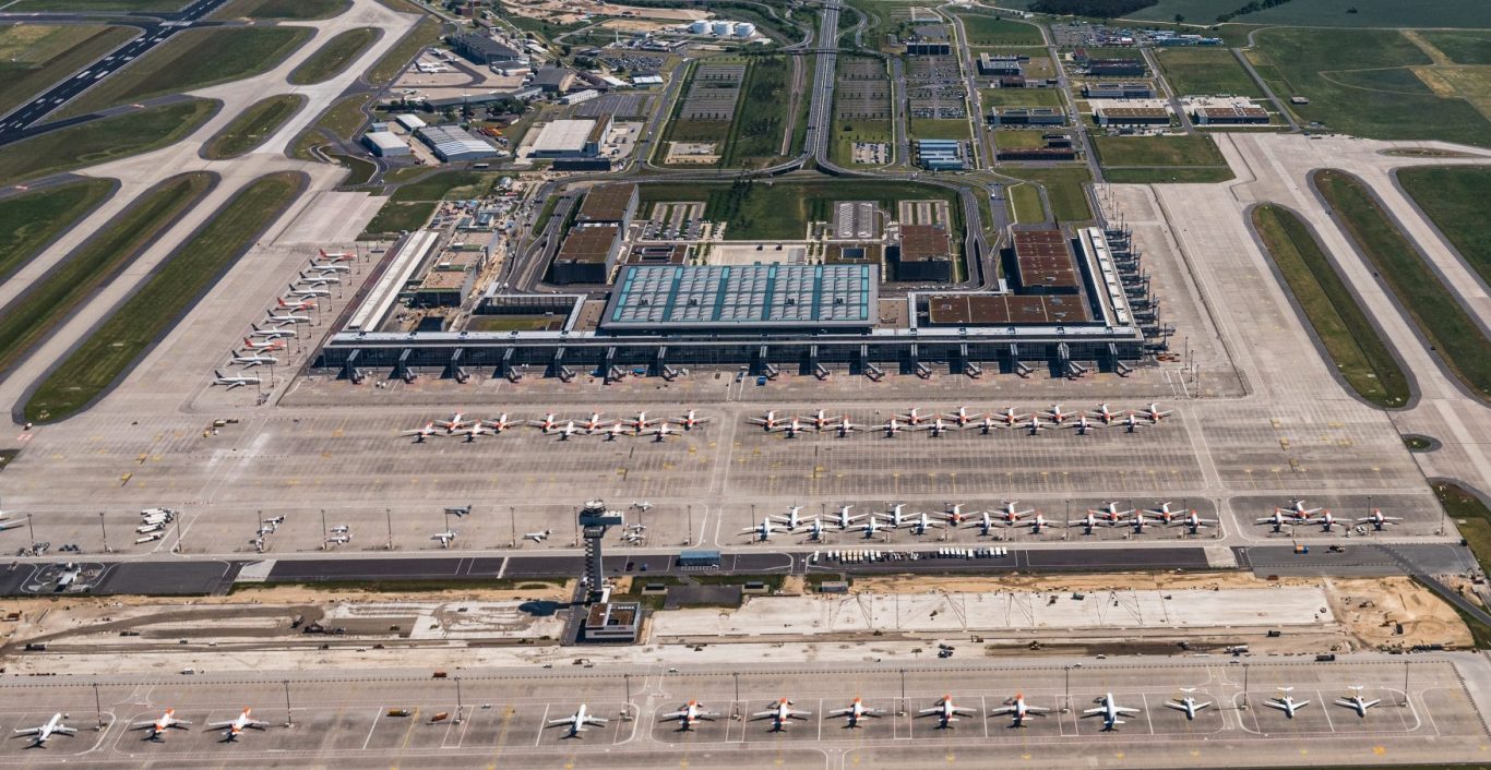 Luftaufnahme eines großen Flughafens mit Start- und Landebahnen sowie Parkplätzen.